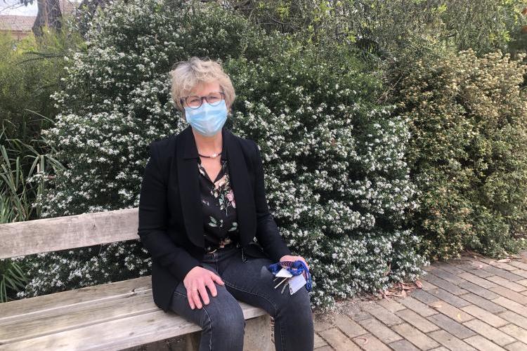 Professor Jo Douglass sits on bench in front of flowering bush