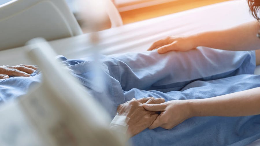 Patient in bed holding another person's hand