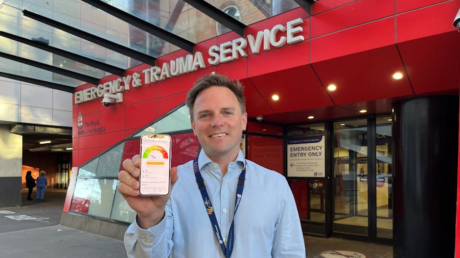 Ben outside ED entrance with emergency wait times dashboard displayed on his phone