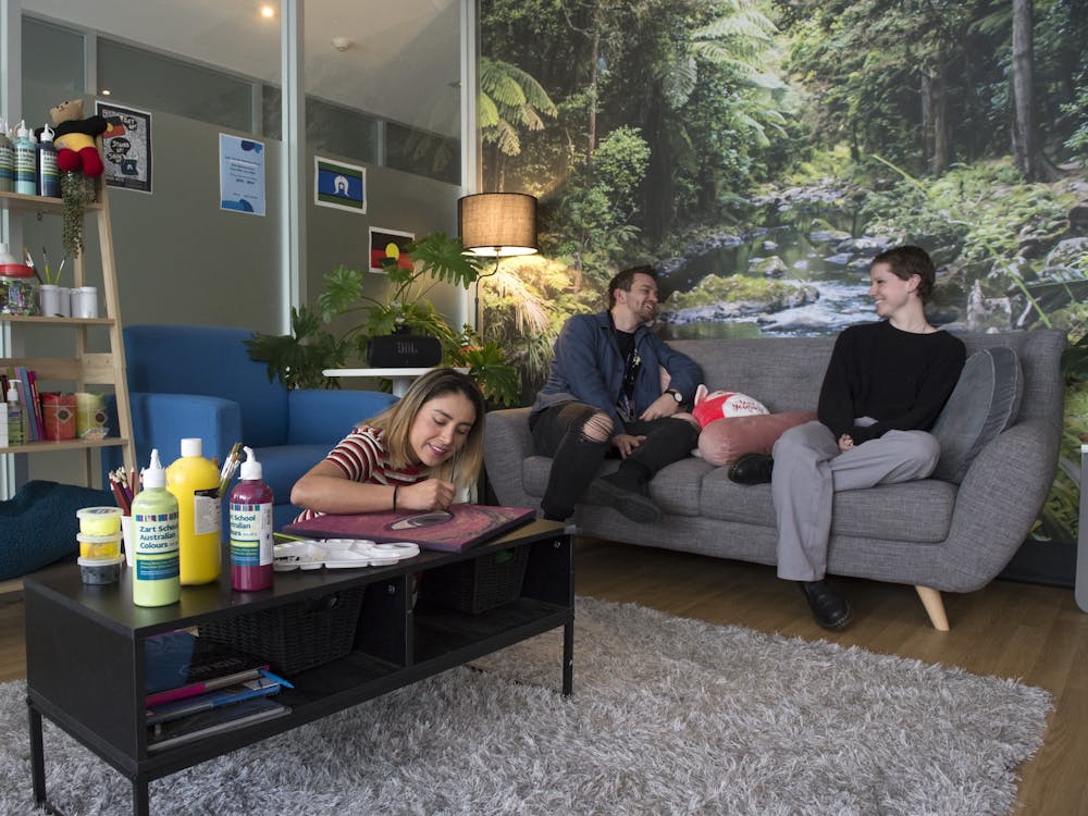 Visitor paints while another talks to a peer worker on a couch at Safe Haven